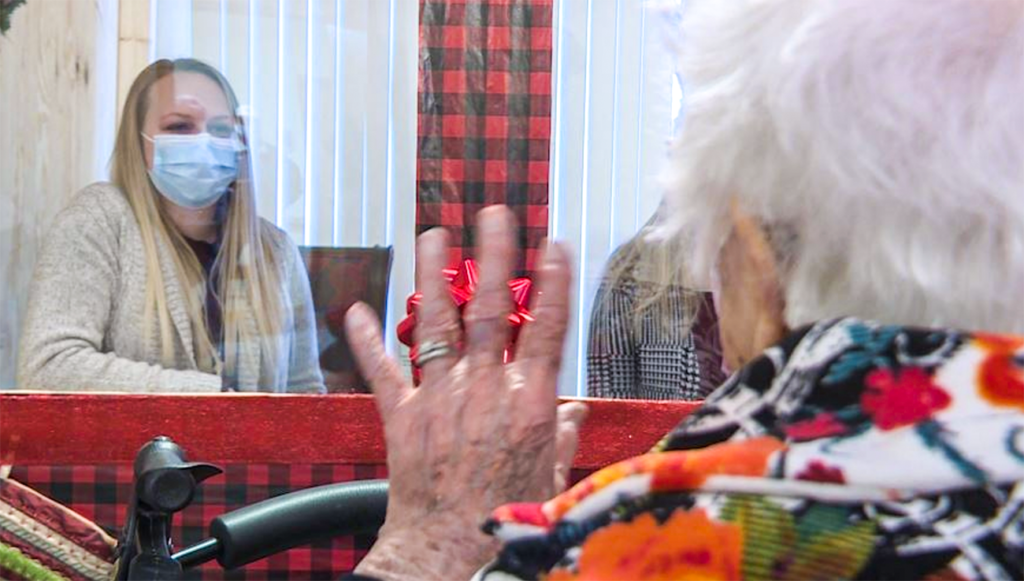 Senior resident visiting with a family members who are sitting in the Visiting Booth