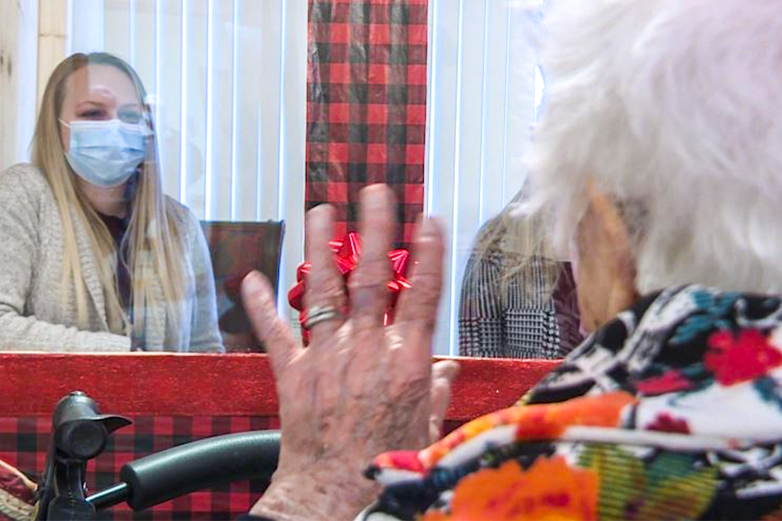 Screen Shot 2020-12-28 at 5.00.48 PM Senior resident visiting with a family members who are sitting in the Visiting Booth