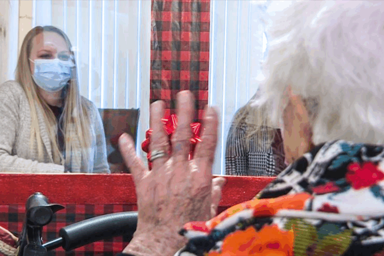 Senior resident visiting with a family members who are sitting in the Visiting Booth